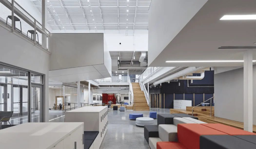 Open office atrium with tiered seating, a wood staircase, and red and blue accents.