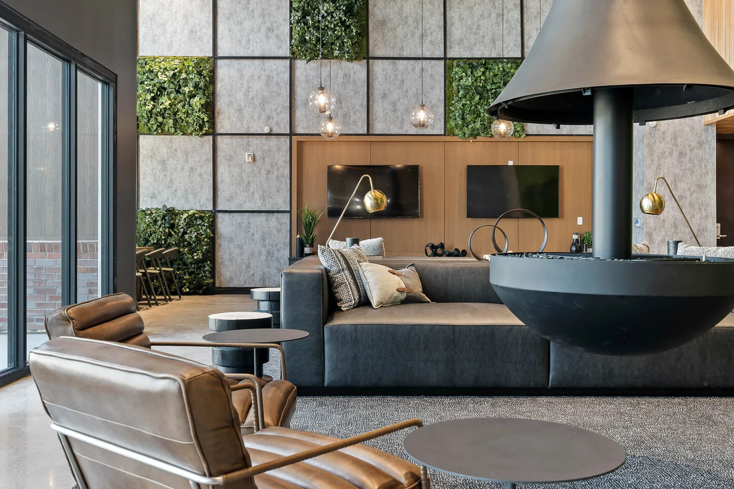Modern lounge with a central black fireplace, gray seating, and living-wall panels.