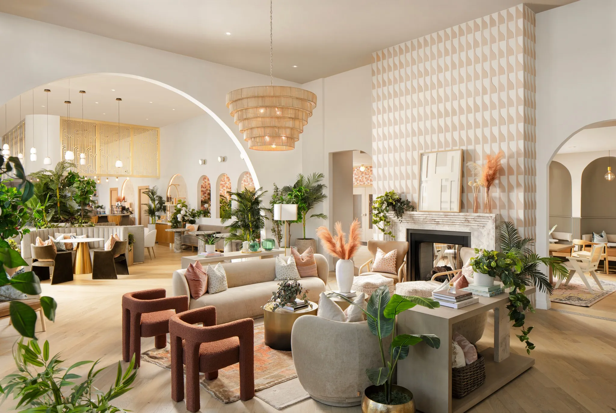 Large cream-and-blush lounge with arched openings, a fireplace, layered seating, and abundant plants.