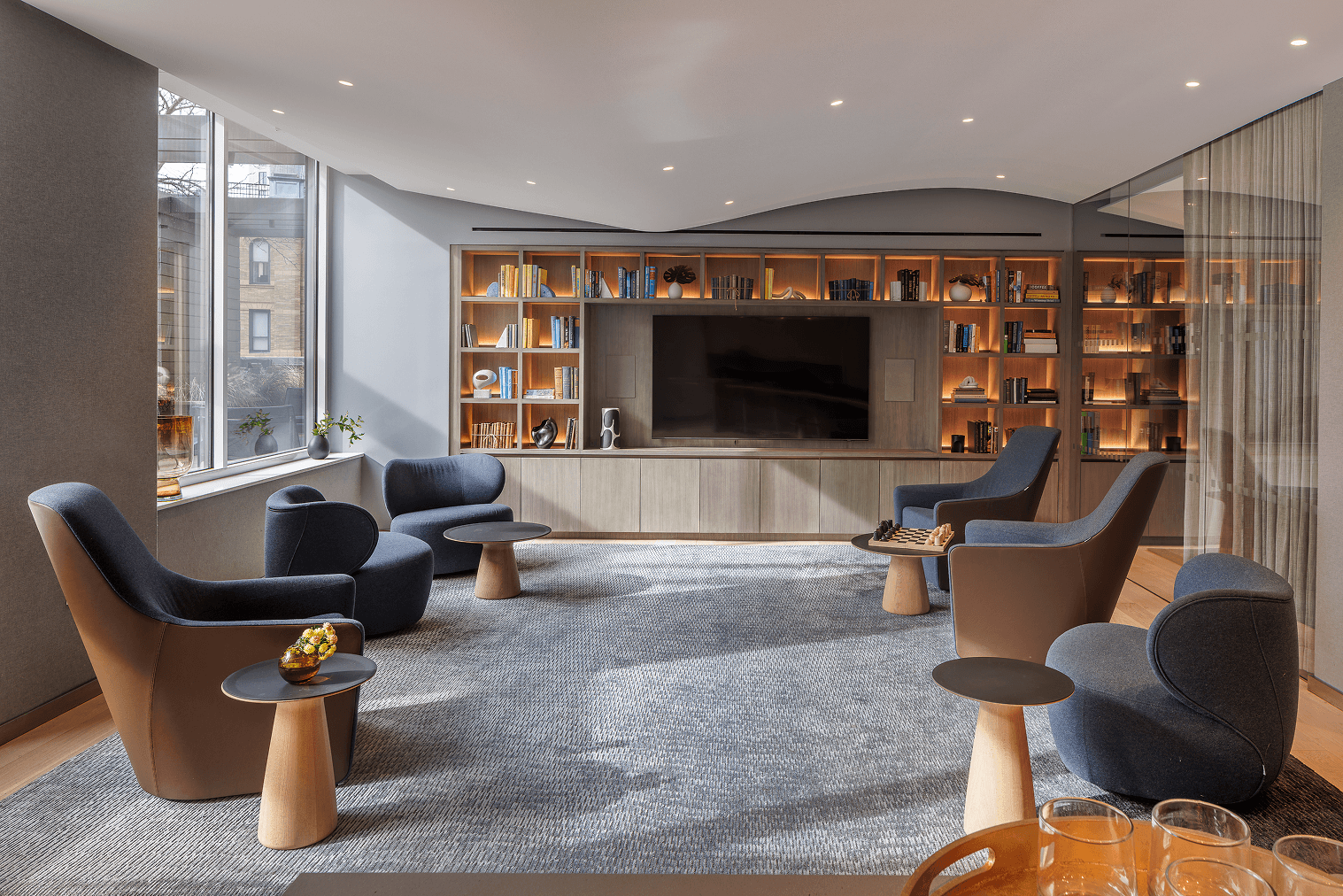 Contemporary lounge with blue armchairs and an illuminated built-in bookcase.