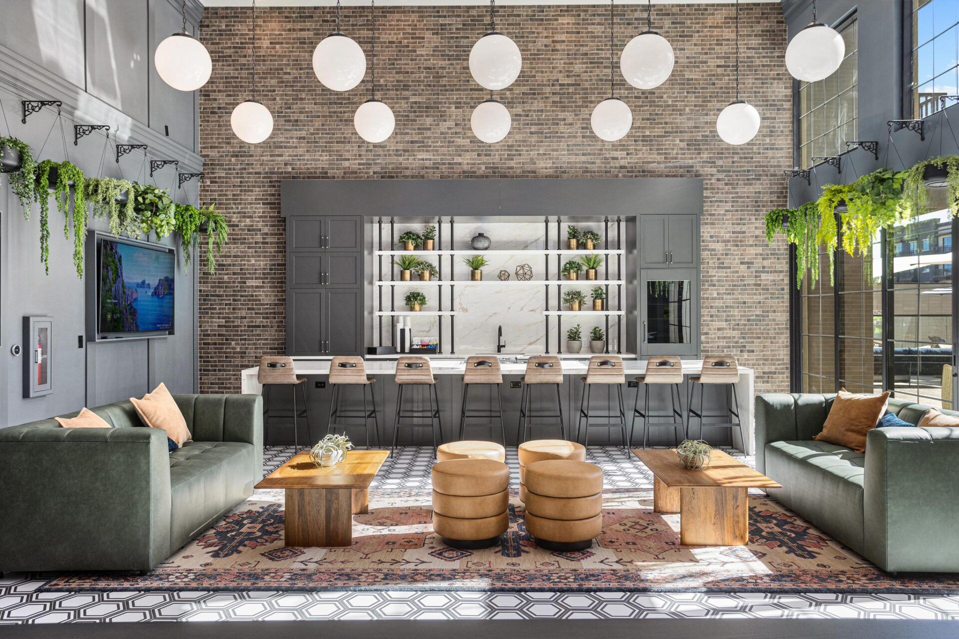 Double-height lounge with green sofas, a long bar, a brick wall, and globe pendant lights.