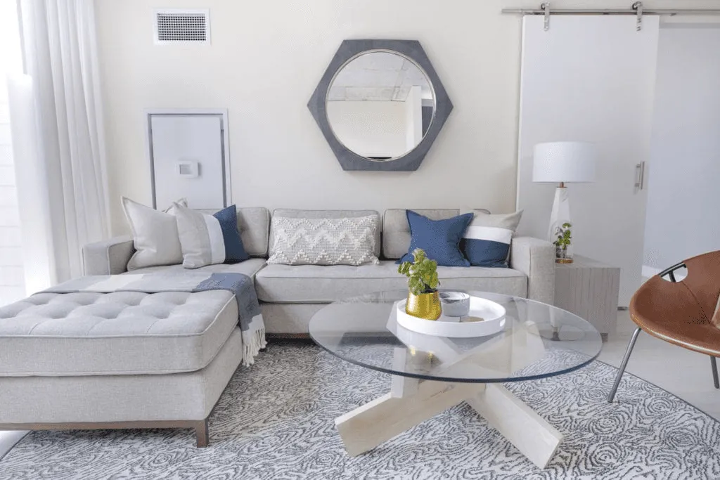 Finished living room with a gray sectional, glass coffee table, and blue accents.
