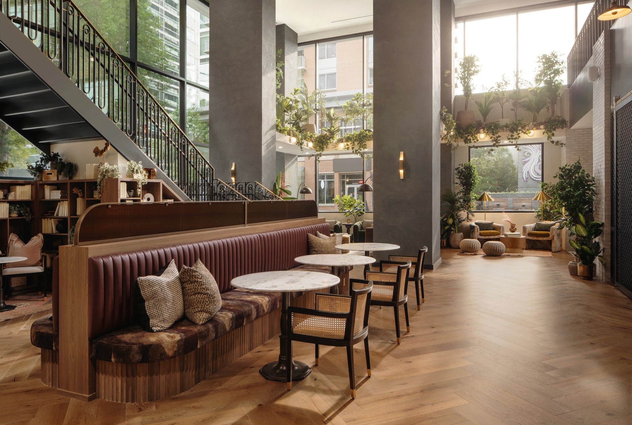 Plant-filled, double-height lobby with banquette seating, café tables, and a staircase.
