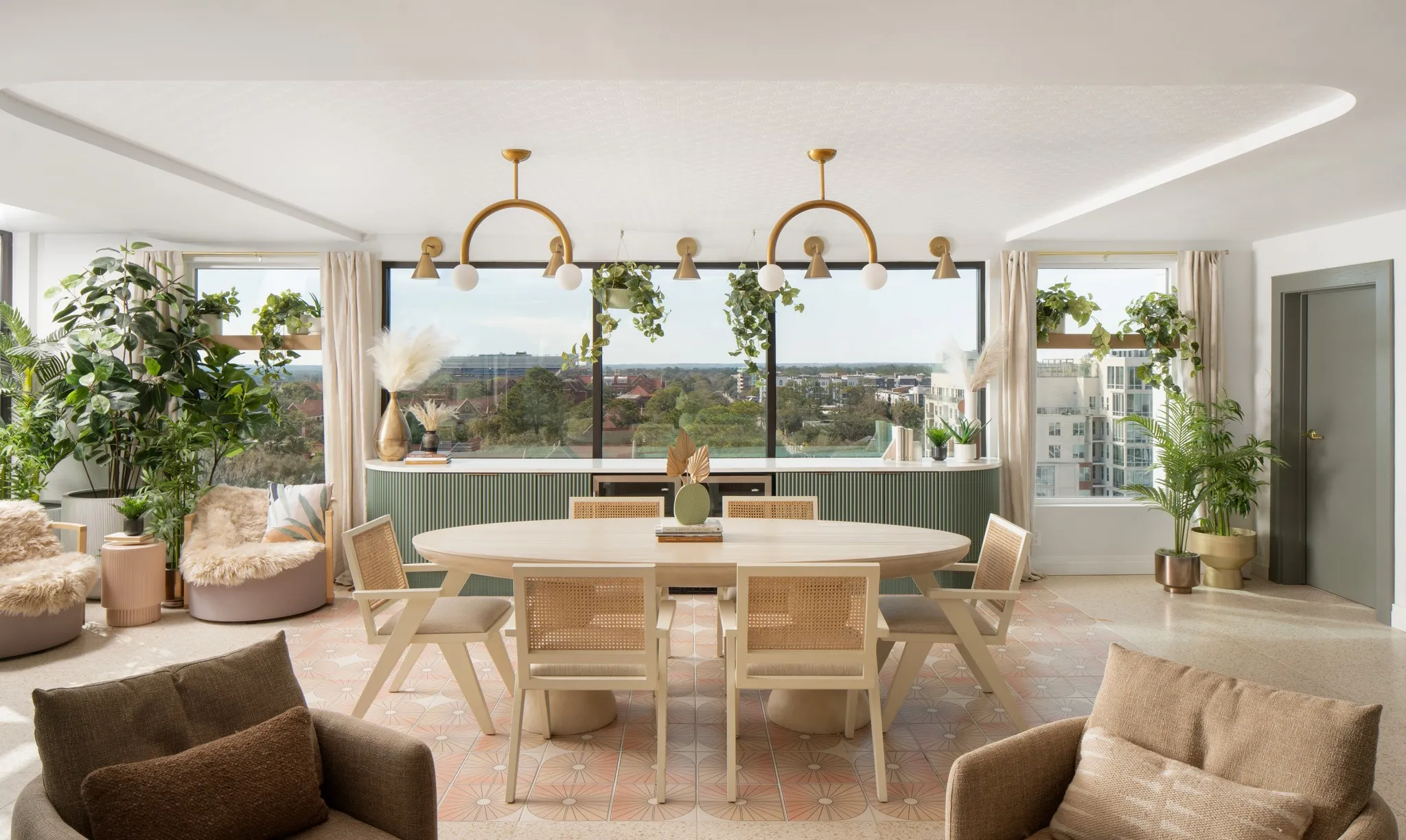 Bright dining and lounge area with a city view, pale wood furniture, and abundant plants.